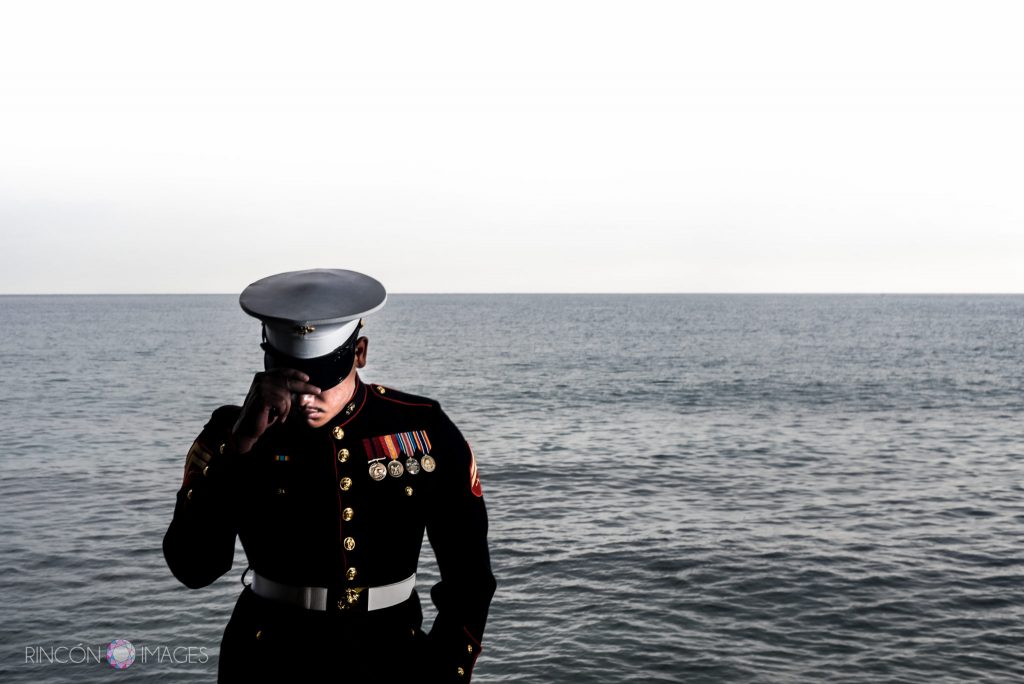 Marine wearing his uniform standing in front of the ocean tipping his hat down.