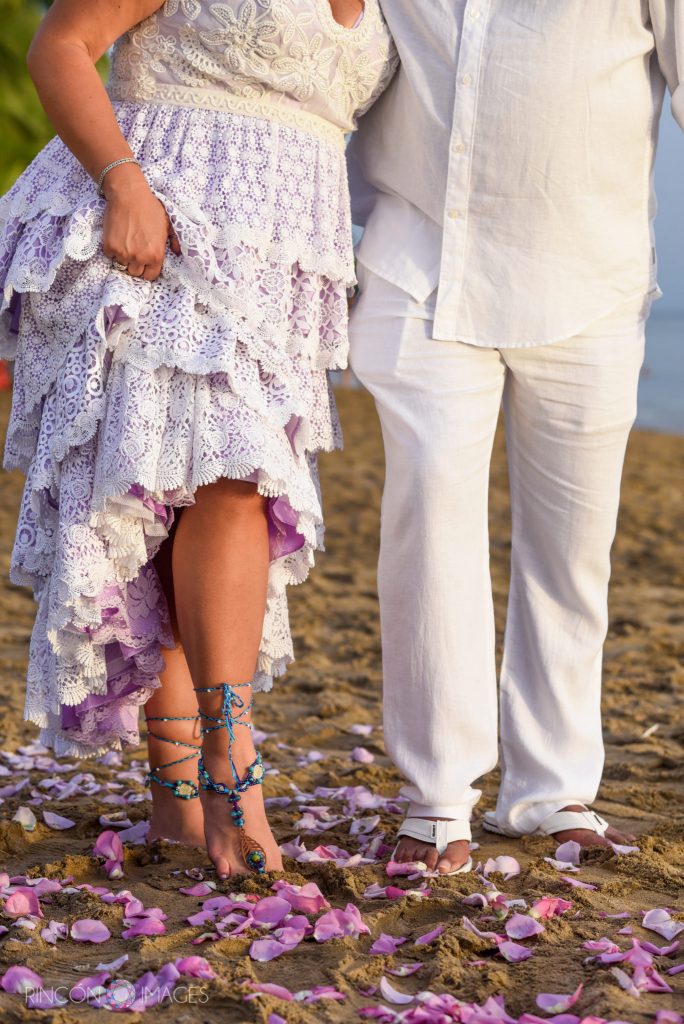 The brides feet standing next to the groom with pink rose petals on the sand.