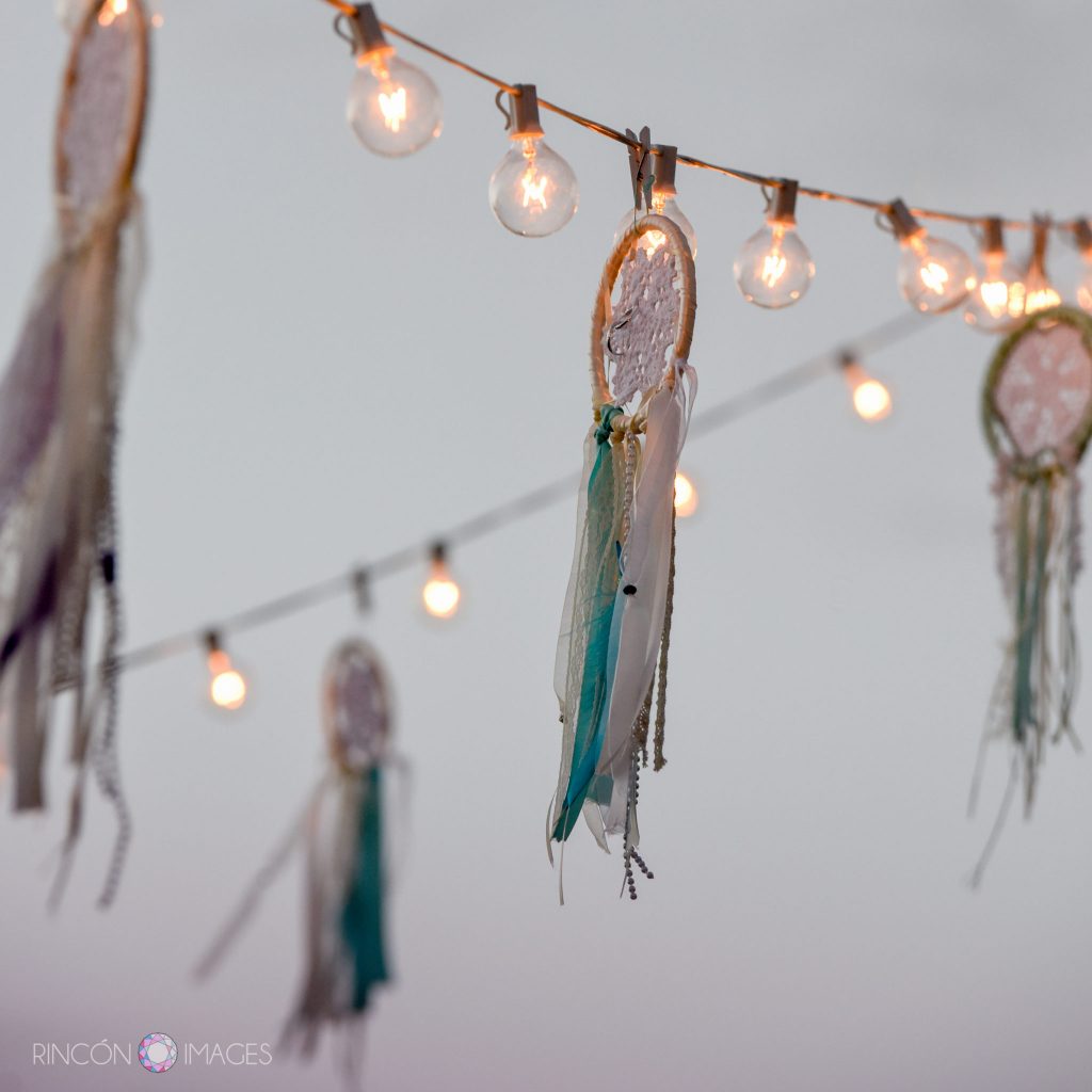 Hand made dreamcatcher wedding decorations hanging from outdoor string lights at sunset during the wedding reception.