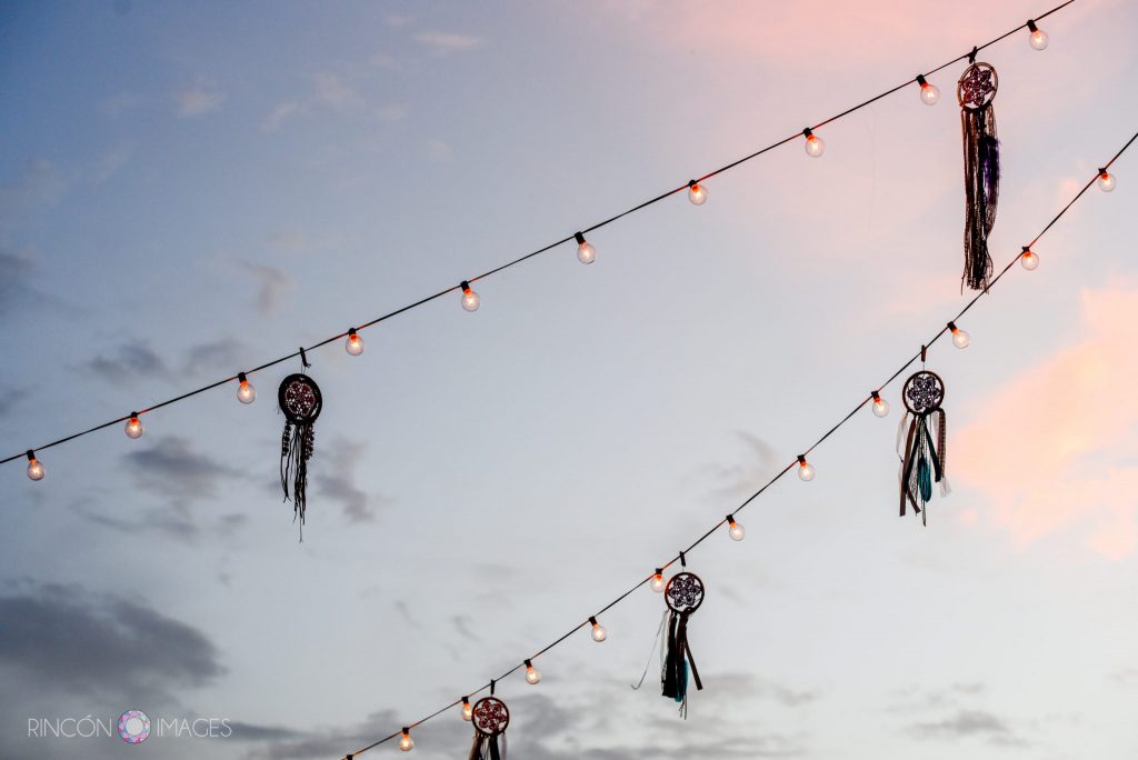 Sunset sky with silhouetted dreamcatcher decorations and outdoor string lights.