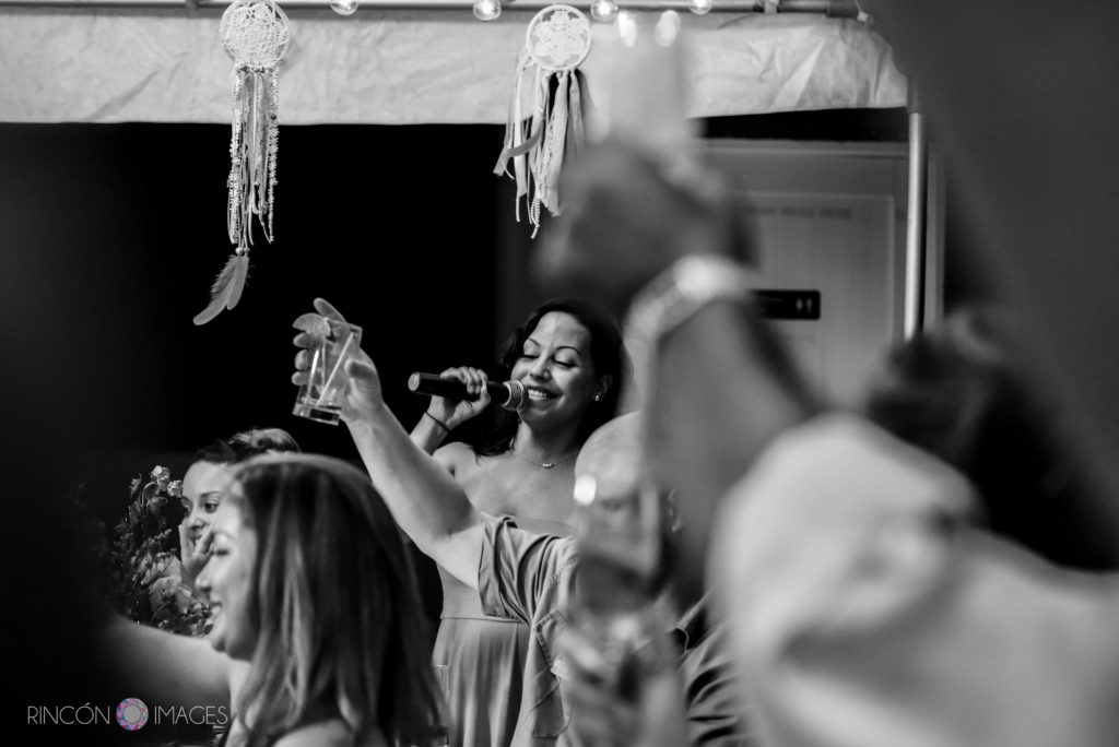 Black and white photograph of the maid of honor giving a toast on the microphone while guests hold up their glasses.